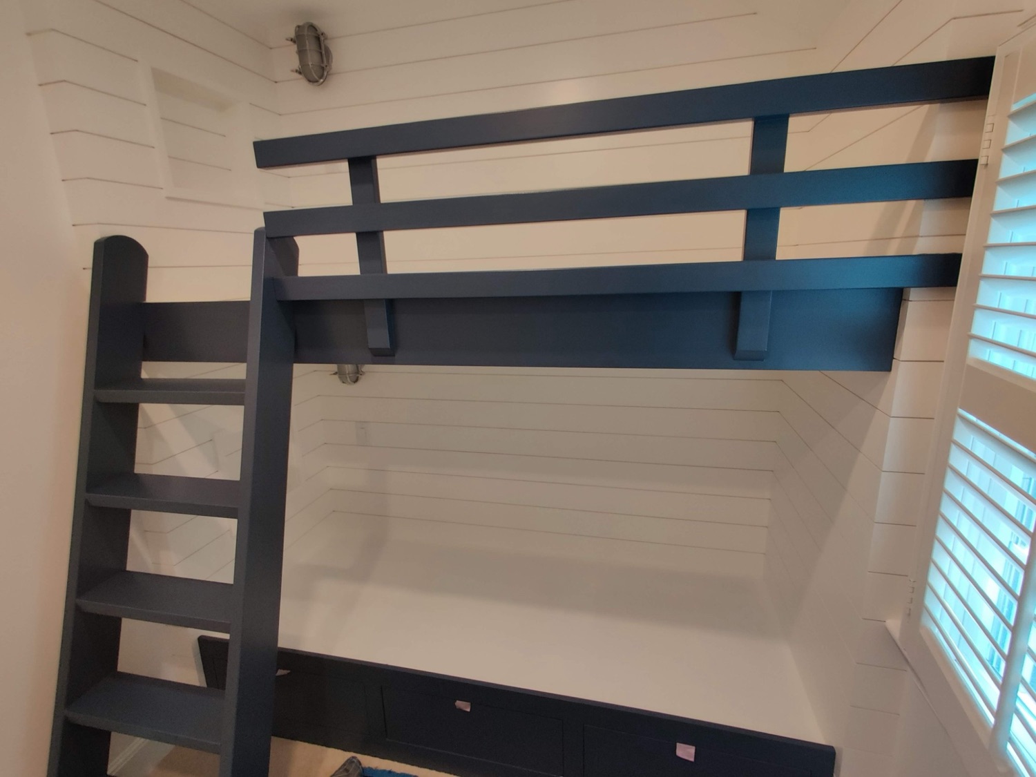 Custom navy loft bunk bed with ladder and shiplap walls in a Cape Cod kids' room